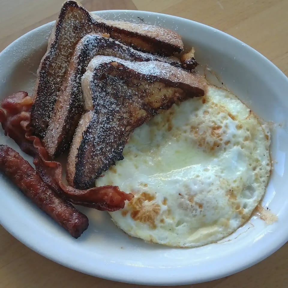 Ever's Diner breakfast plate with powdered sugar French toast, fried eggs, bacon, and sausage.
