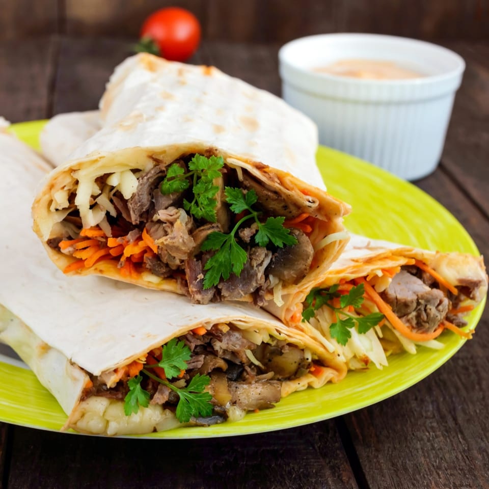 Three shawarmas filled with meat, cabbage, carrots, and parsley, on a green plate with sauce.
