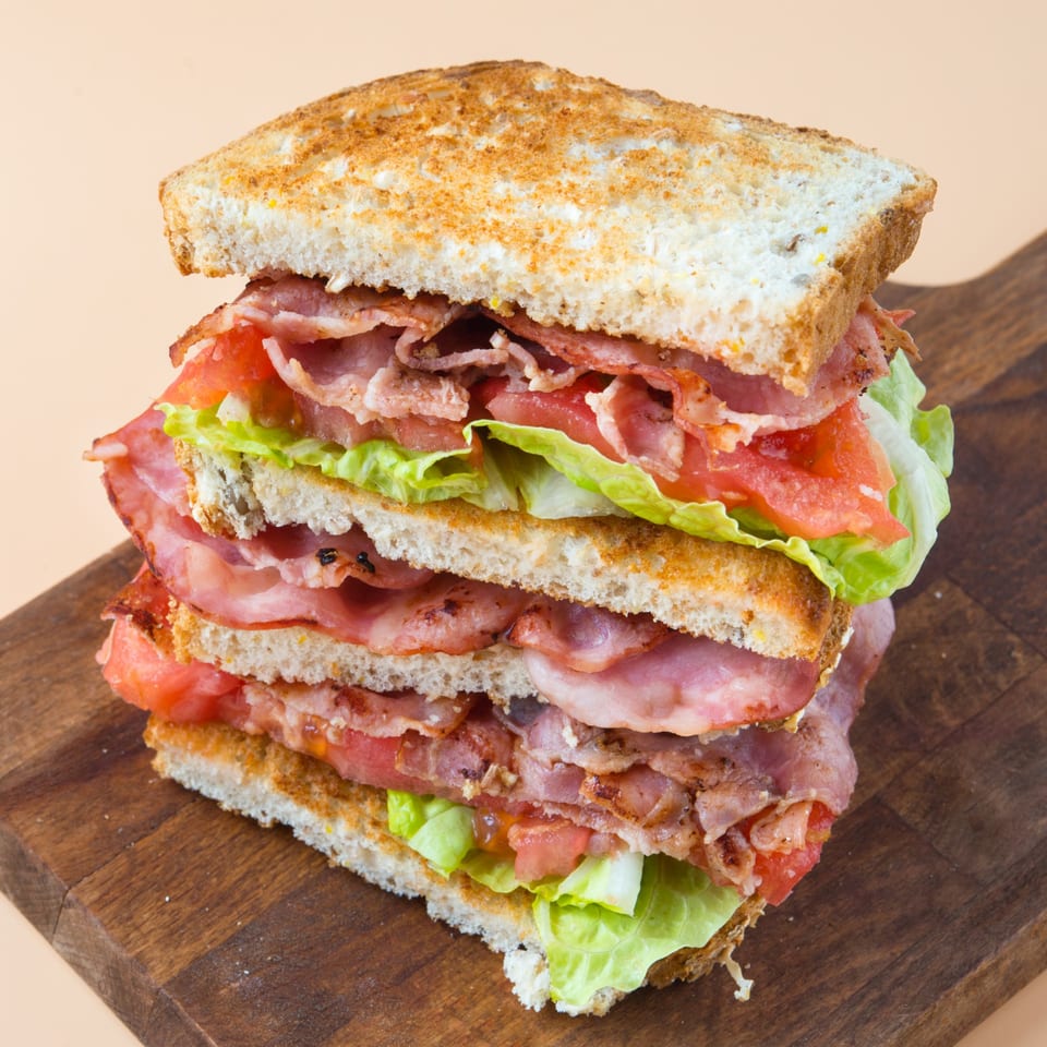 A tall, stacked bacon, lettuce, and tomato sandwich on toasted bread, served on a wooden board.